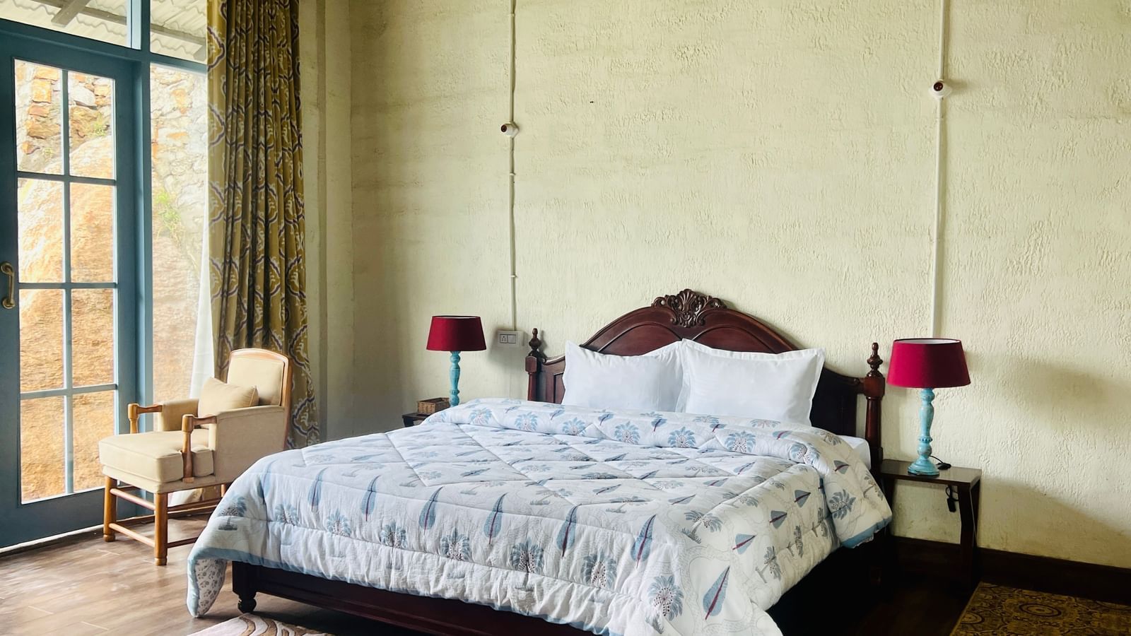 Bedroom at Faraway Cottages, Auli - one of the best Hotels in Badrinath Near Temple -  with a large bed, bedside lamps, patterned bedding, chair, and tall window with curtains.